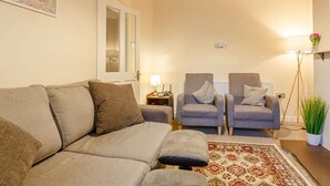 Ein Wohnzimmer mit einer Couch, zwei Sesseln, einem gemusterten Teppich, einer Lampe und einer Topfpflanze.
