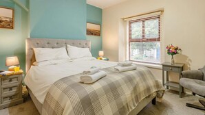 Ein Schlafzimmer mit Bett, Nachttischen, einem Sessel, einem Fenster mit Jalousien und Bildern an den Wänden.
