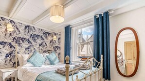Quarto com cama, mesa de cabeceira, janela com cortinas, espelho e vista para edifícios.