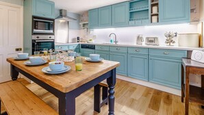 Uma cozinha com armários azul-turquesa, uma mesa de madeira com louças e um micro-ondas.