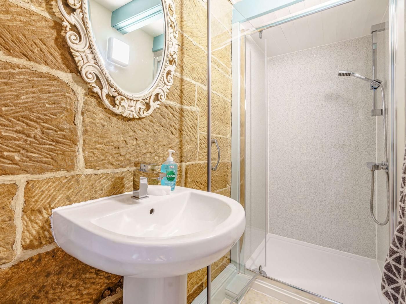 Un bagno con parete in pietra, lavandino bianco, specchio e cabina doccia in vetro.