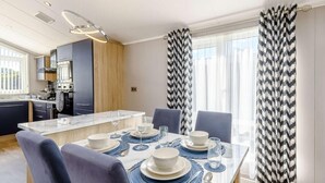 Eine moderne Küche mit integrierten Geräten, ein Essbereich mit einem Marmortisch, gedeckt für vier Personen, und große Fenster mit gemusterten Vorhängen.