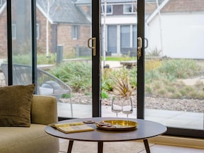 A modern room with a sofa, a small round table, and a glass door leading to a garden. - 2 Bed in Porthcawl (oc-89696) (Porthcawl)