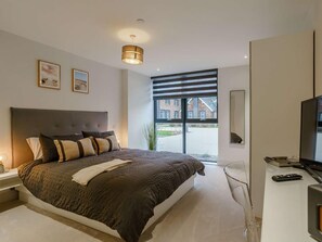 Une chambre moderne avec un grand lit, une télévision et une fenêtre donnant sur un immeuble.