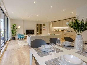 A modern living room with a sofa, dining table set for two, and a kitchen in the background. - 2 Bed in Porthcawl (oc-89696) (Porthcawl)