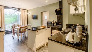 Une cuisine moderne dotée d’un îlot central, d’un coin repas avec une table et des chaises, et offrant une vue sur un jardin grâce à une grande fenêtre.
