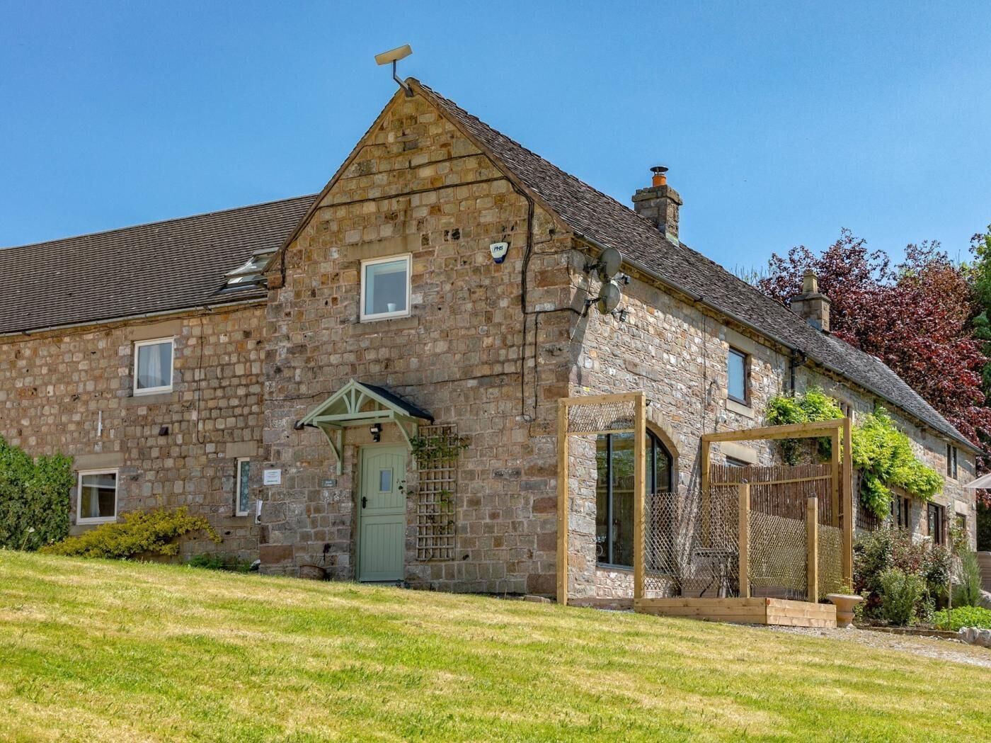 A stone building with a green door, a small porch, and a fenced outdoor area.
