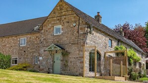 Un bâtiment en pierre avec une porte verte, un petit porche et un espace extérieur clôturé.