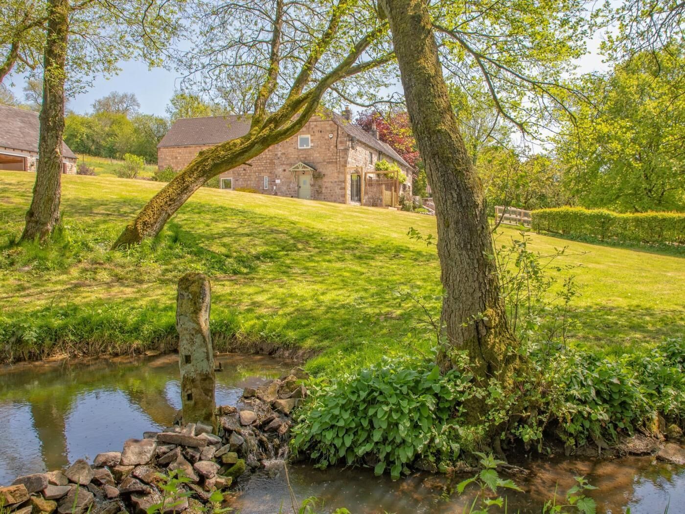 A rural landscape with a stone house, a stream, and a grassy field.