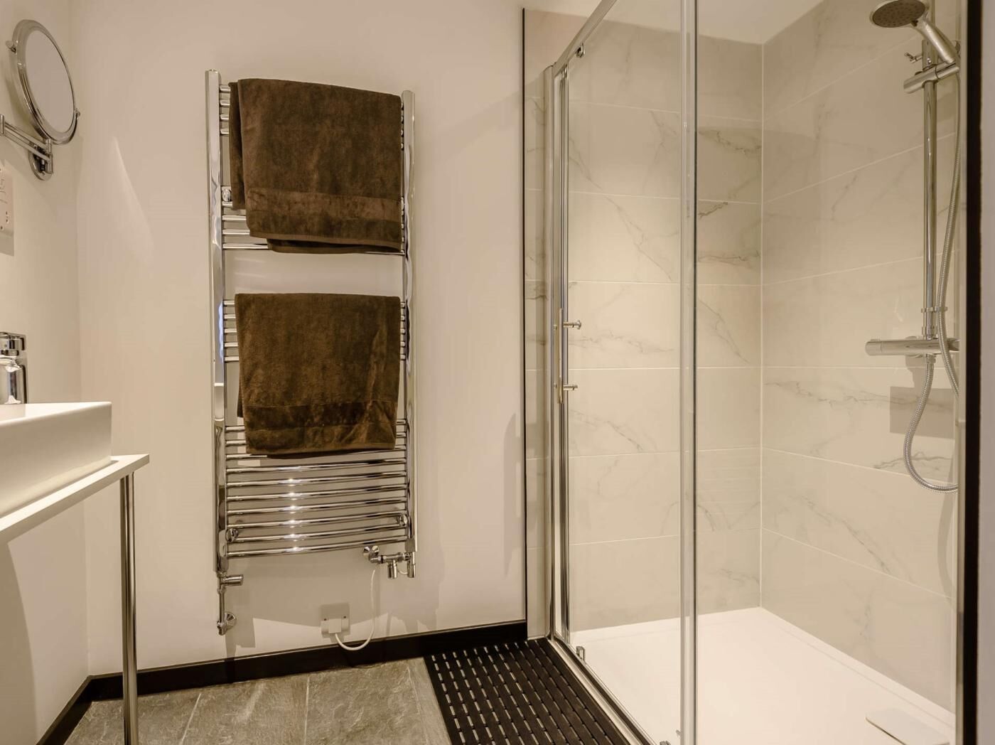 A modern bathroom with a glass shower enclosure, a towel rack with two towels, and a white sink.