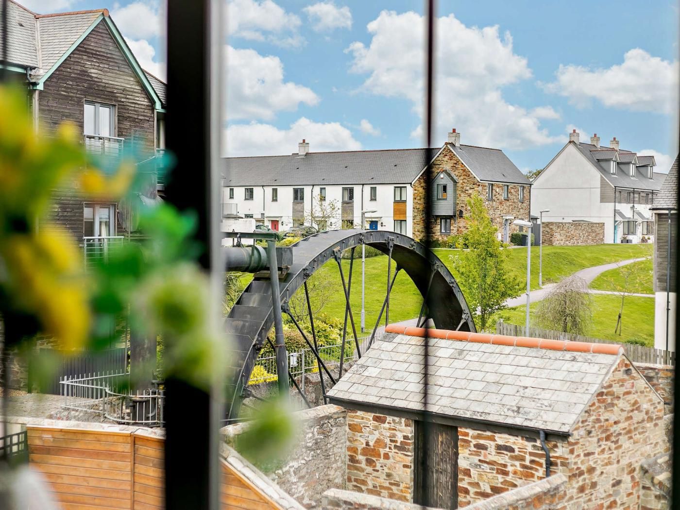 A view of a residential area with a large water wheel, houses, and a stone building.
