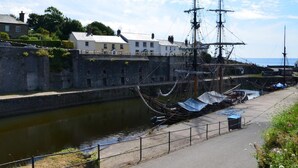 Une promenade en bord de mer avec un navire historique amarré, un mur de pierre et des bâtiments le long de la côte.