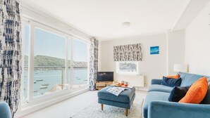 Ein Wohnzimmer mit großem Fenster, einer Couch, einem Fernseher und Blick auf das Meer.