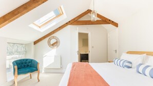 Ein Schlafzimmer mit einem großen Bett, einem blauen Sessel, einer Holzbalkendecke und einem Oberlicht.