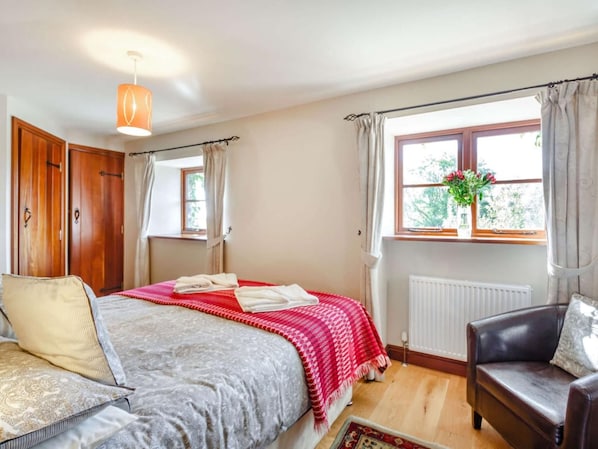 Ein Schlafzimmer mit einem Bett, einem Sessel, einem Fenster mit Vorhängen und einer Heizung.