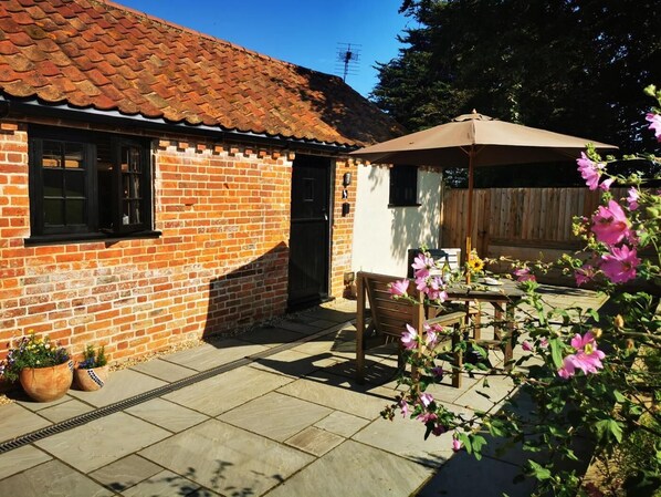 Une maison en briques avec un toit en tuiles, une porte en bois et une terrasse avec une table et des chaises.