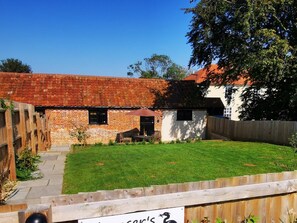 Une maison en briques avec un toit recouvert de tuiles rouges, une cour arrière clôturée et une terrasse en bois.