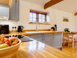 Une cuisine avec un plan de travail en bois, un évier, une fenêtre avec des stores et un coin repas avec des chaises.