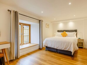 A bedroom with a bed, a bedside table, a lamp, a window with curtains, and a view of the outside. - 2 Bed in Bideford (oc-89336) (Monkleigh)