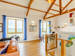 A spacious living area with a wooden ceiling, large windows with blue curtains, a leather sofa, and a dining area with a table and chairs. - 2 Bed in Bideford (oc-89336) (Monkleigh)