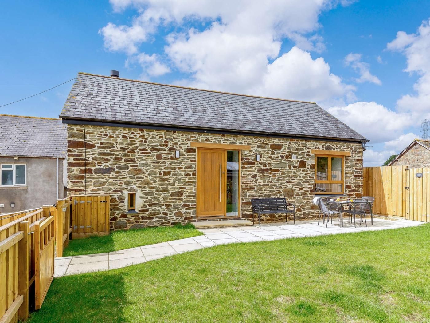A stone building with a wooden door, a small window, and a patio with a table and chairs.