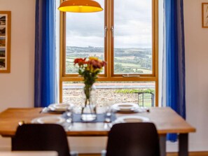 A dining table set with plates and a vase of flowers, positioned in front of a window with a view of a landscape. - 2 Bed in Bideford (oc-89336) (Monkleigh)