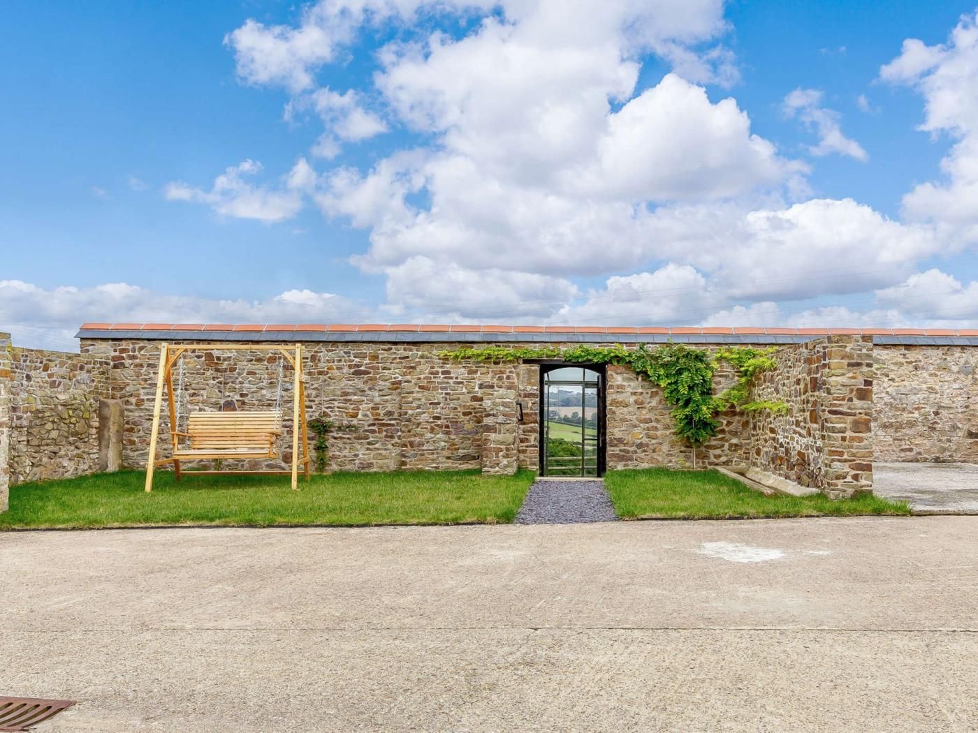 A stone building with a wooden swing, a door, and a view of the countryside.