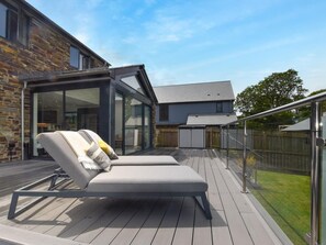 A deck with two lounge chairs, a glass-enclosed patio area, and a view of a house with a stone facade. - 4 Bed in Bude (oc-89355) (Poughill)