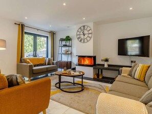 A modern living room with a fireplace, a large wall clock, and a flat-screen TV. - 4 Bed in Bude (oc-89355) (Poughill)