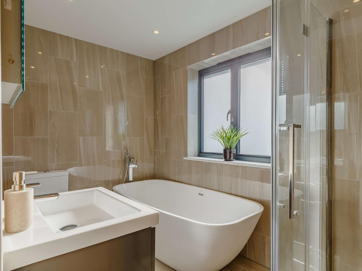 Ein modernes Badezimmer mit einer freistehenden Badewanne, einem Fenster mit Pflanze und einer Duschkabine aus Glas.
