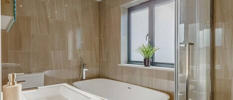 A modern bathroom with a freestanding bathtub, a window with a plant, and a glass shower enclosure.