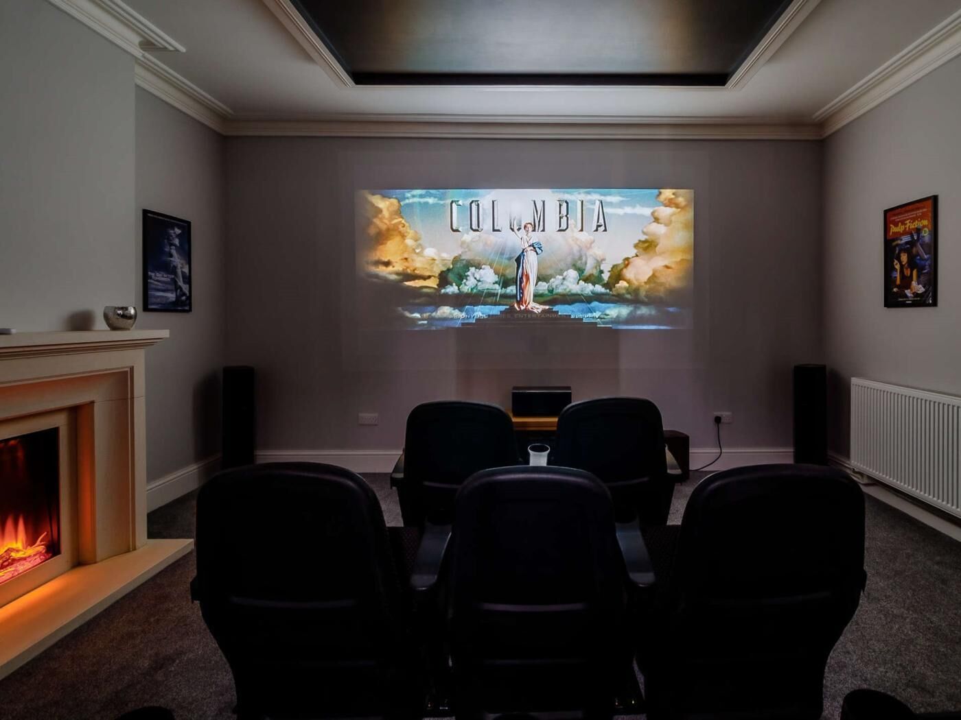 A conference room with a fireplace, a projector screen displaying 'COLombia,' and a poster on the wall.
