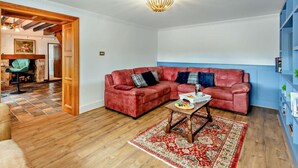 A living room with a red sofa, a wooden coffee table, a patterned rug, and a blue wall. - 3 Bed in Holywell (oc-89614) (Gorsedd)