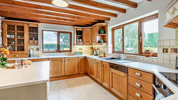 A kitchen with wooden cabinets, a large window, and a hanging light fixture. - 3 Bed in Holywell (oc-89614) (Gorsedd)
