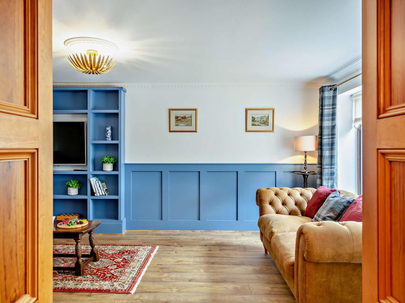 A living room with a blue accent wall, a tufted sofa, a wooden coffee table, a red patterned rug, and a ceiling light fixture.