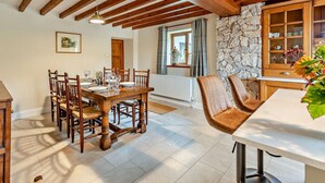 A dining area with a wooden table and chairs, a stone wall, and a window with curtains. - 3 Bed in Holywell (oc-89614) (Gorsedd)
