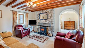 A cozy living room with a stone fireplace, leather sofas, and wooden beams on the ceiling. - 3 Bed in Holywell (oc-89614) (Gorsedd)