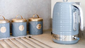 Tre blå förvaringsbehållare med gyllene lock och handtag, en silverfärgad vattenkokare och ett metallställ.