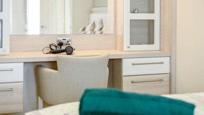 Ett hotellrum med ett skrivbord i trä, en stol, en spegel och en säng med en turkosfärgad kudde.