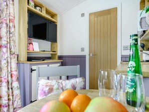 Quarto com televisão, prateleira de madeira, porta e mesa com frutas e copos.