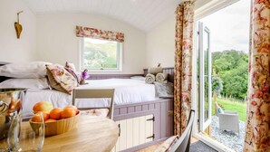 Ein Schlafzimmer mit einem Bett, einem Fenster mit Blick auf Grünflächen, einem Tisch mit Früchten und einem Stuhl.