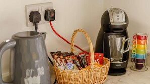 Un ripiano della cucina con un bollitore, una macchina per il caffè, una tazza e un cestino di cialde per caffè.