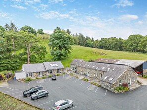 A stone building with multiple rooms, a parking lot, and a green landscape with trees.