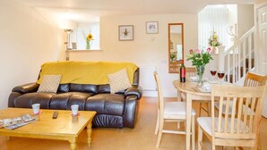A living room with a brown leather sofa, a yellow throw, a wooden coffee table, and a dining area with a white table and chairs. - 1 Bed in Bala (oc-89369) (Llandderfel)