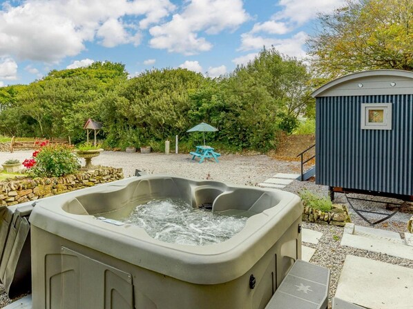 Ein Whirlpool mit Steinrand, eine kleine Gartenhütte und ein Picknicktisch in einer Gartenanlage.
