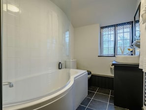 A bathroom with a bathtub, toilet, and window with lace curtains.