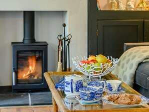 A cozy living room with a wood-burning stove, a fruit bowl, blue and white tea set, and a plate of cookies.