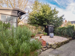 A house with a stone wall, a black shed, and a garden with various plants and a small water feature. - 1 Bed in Bridport (oc-89687) (Bridport)