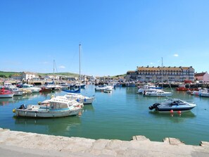 A marina with various boats docked, a clear sky, and buildings in the background.