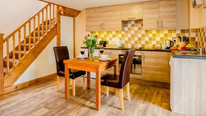A kitchen with wooden cabinets, a dining table with chairs, a wooden staircase, and a checkered backsplash. - 1 Bed in Bala (oc-89368) (Llandderfel)